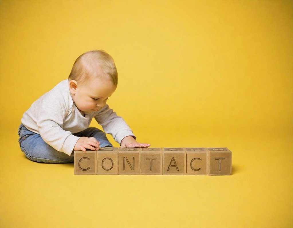 A baby in a white top is playing with blocks spelling "CONTACT" on a yellow background.